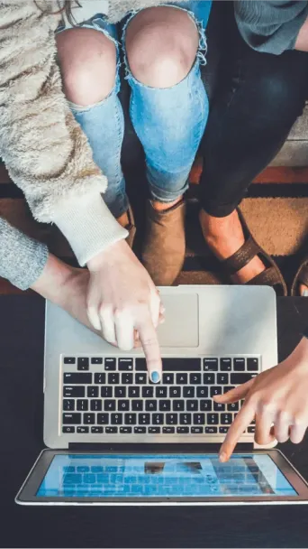 Three people sitting on a couch pointing at a laptop.